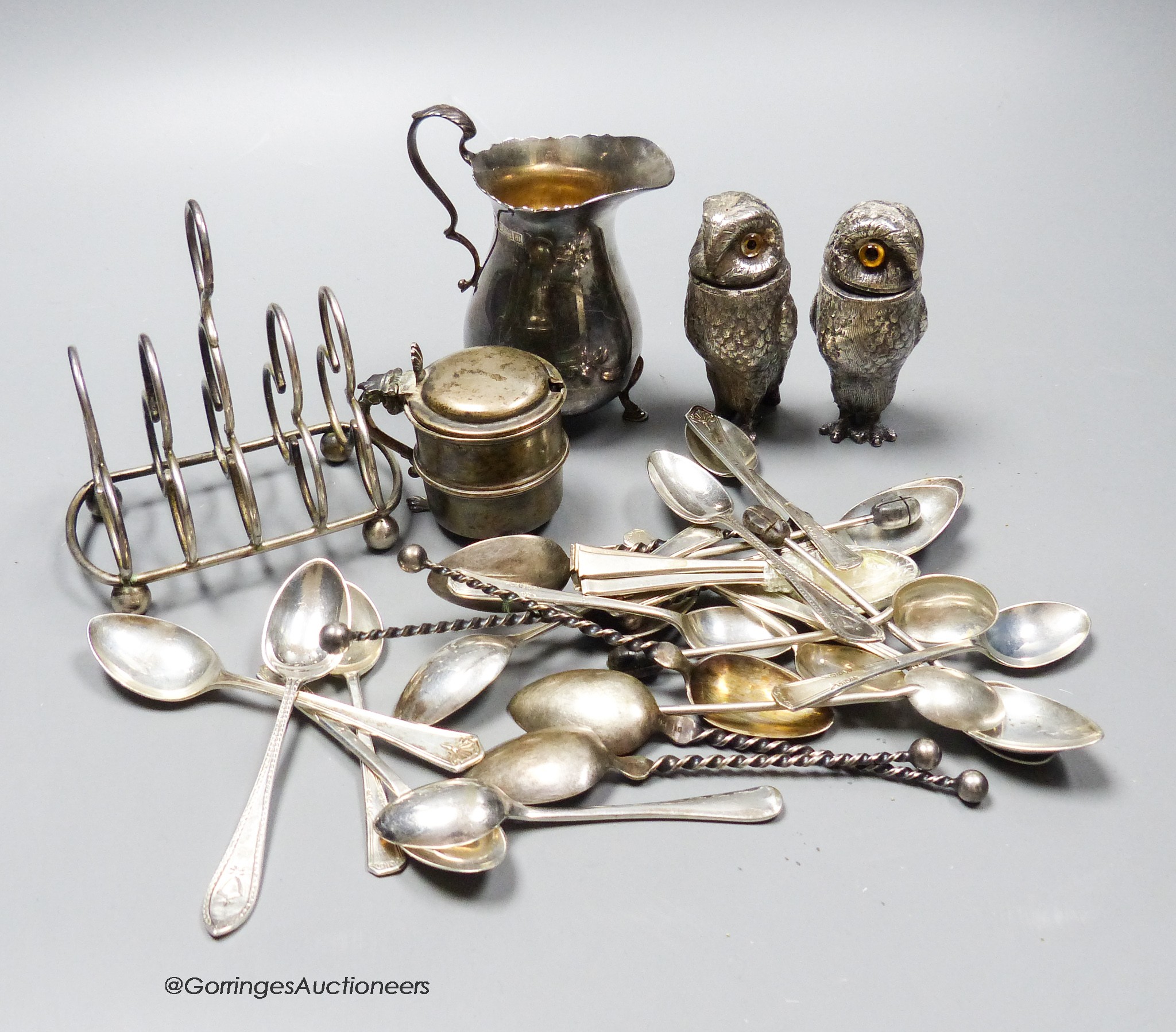 Small silver including a silver five bar toastrack, a silver mustard, a silver cream jug, assorted teaspoons and a pair of base metal owl condiments(a.f.)